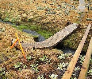 Broken bridge across Sawyer Creek near Green Gorge. The wooden slatted narrow bridge is bent at an angle over the creek where the timber supports have been broken