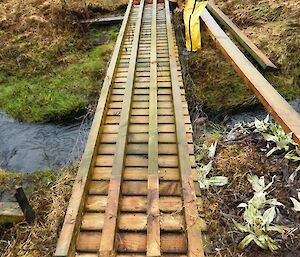 David carrying out repairs of the bridge. The bridge is upside down with Dave at one end securing the four long pieces of timber struts