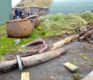 Heritage area on station. Old timbers, machinery and three try pots lie amongst the moss, dirt and other vegetation in an area between the Green store and the old post office building