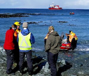 Arriving at Landing Beach. Two newly arrived expeditioners, Dana and Jack stand on the beach with Steve and Marty, while a IRB is held on the water by shore crew as it is unloaded. L'Astrolabe and one of the other IRB’s can be seen in the background