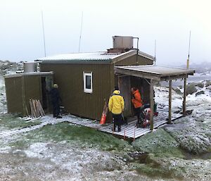 Arriving at Bauer Bay hut. picture taken from just above the hut shows a a light cover of snow over the hut and landscape, while Wim, Dominic and Mark check the hut. There is snow falling