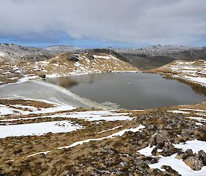 Taken from a hill above Emerald Lake, we see a snow covered landscape with Dominic on the inflatable dingy in the middle of the lake where at the intersection of two yellow ropes that are stretched, perpendicular to each other, across the lake. Mark, Wim and the equipment can be seen on the right shore of the lake