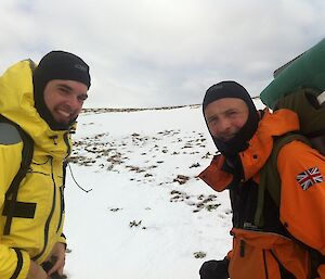Wim, in a yellow weather proof jacket, and Dominic, in a orange jacket, on the snow covered plateau, both carrying packs loaded with the coring kit