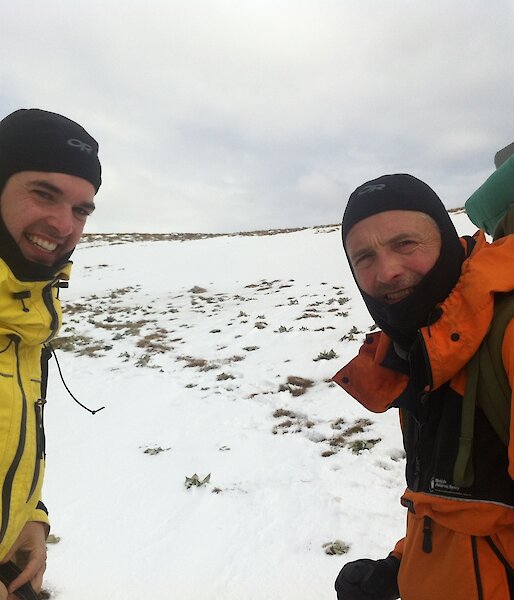 Wim, in a yellow weather proof jacket, and Dominic, in a orange jacket, on the snow covered plateau, both carrying packs loaded with the coring kit