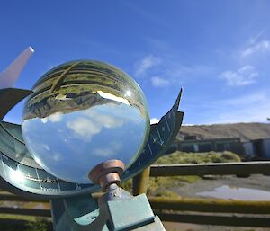 Campbell-Stokes sunshine recorder. A glass ball which focus sunlight to burn onto a card. The view in the ball is the inverted and concave distorted image of the escarpment, station buildings and log fence of the weather enclosure