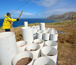 At the Wireless Hill Orchard site — Clive, using a piece of timber to hammer down and secure the final tubes into place within the steel frames. The east coast and ocean provide a scenic backdrop