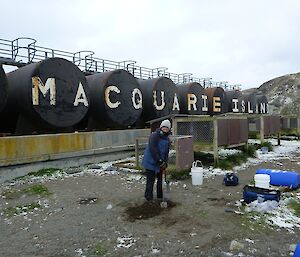 Ingrid taking soil samples from the ground in front of the fuel tanks in the fuel farm enclosure. ‘MACQUARIE ISLAND’ is painted on the fuel tanks in white paint