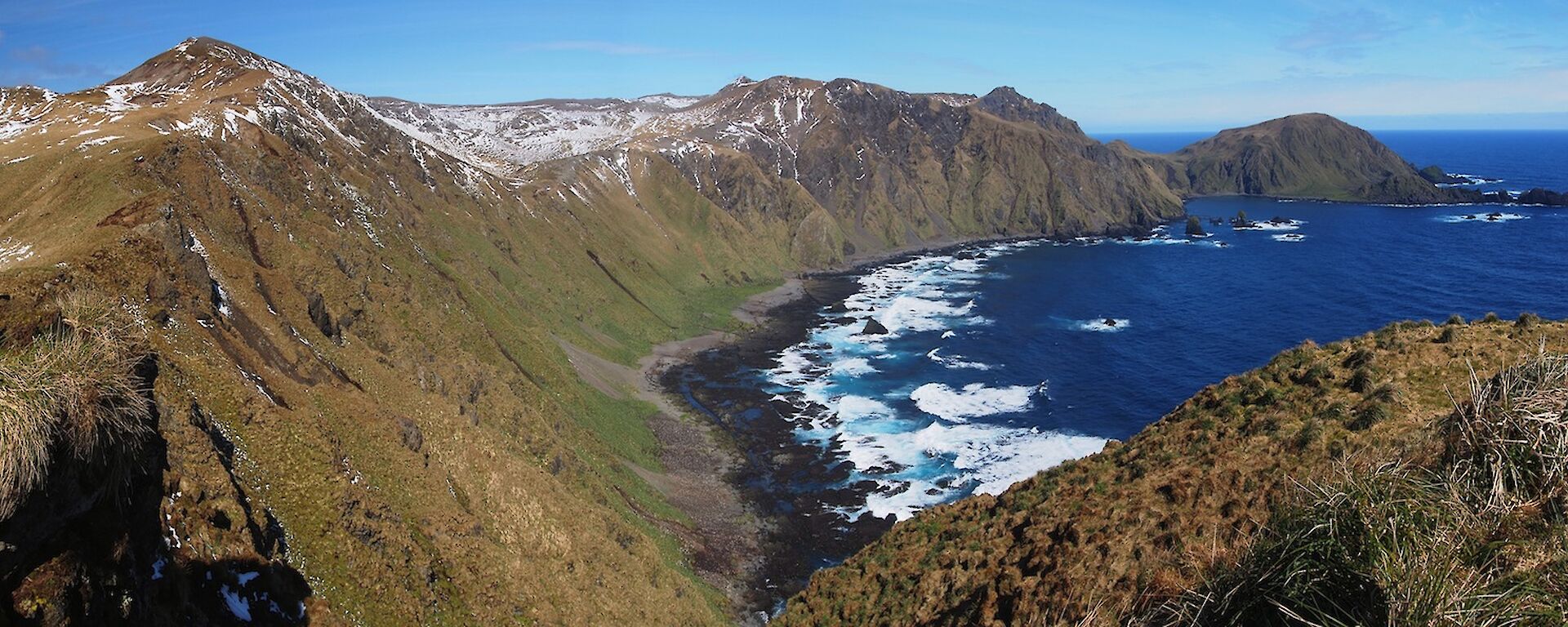 A panorama showing Kate, in the far right of picture, standing on a grassy knoll at the edge of the escarpment getting her bearings by looking across the bay with Cape Star on the far left