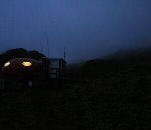 At night Brothers Point hut stands out with interior light bright out of the oval windows looking like two eyes