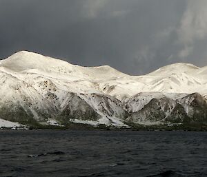 Snow-covered Macquarie Island — the view on Thursday morning from the first tourist ship of the season, the Spirit of Enderby. The white snow covered escarpment is in stark contrast with the darkening sky and the dark ocean water
