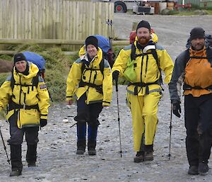 Nat, Ingrid, Jimmy and Marty arrive back at VJM after field training. Nat, Ingrid and Jimmy are wearing the yellow wet weather gear and everyone is carryin a pack (survival) and each have walking poles