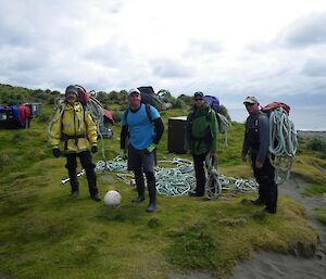 Clive, Josh, Kris and Chris, each with a backpack loaded with pieces of rope, back on the grass besides the Bauer Bay hut