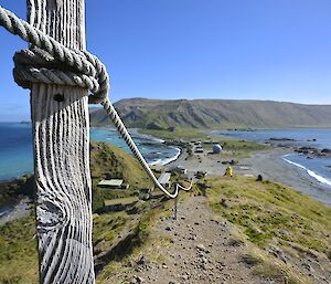 Wireless Hill track, showing a close-up of one of the weathered timber guide rope poles in the left foreground. The view is down the track towards the isthmus and escarpment beyond. The vivid colours of the sky, sea and land are enhanced by the sunny conditions