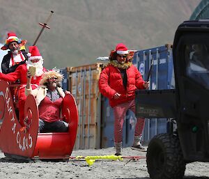Santa Claus and Mrs Claus in red sleigh being towed by the Polaris and with elves following