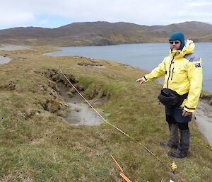 Mike setting up an erosion monitoring site at Major Lake. He is in the foreground with a tape measure lying across a depression of bare earth near the shore of the lake