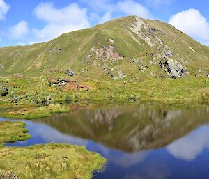 West coast near Eagle Cave. The escarpment, the hill that contains Eagle Cave, the scattered cloud in the bright blue sky are all reflected in a small lake