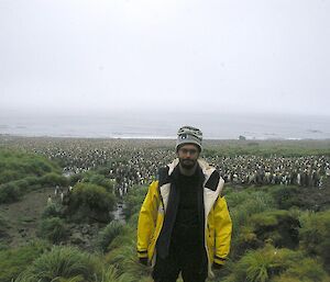 Luis standing amongst the tussock at Luisitania Bay, with the large king penguin colony in the background