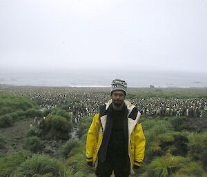 Luis standing amongst the tussock at Luisitania Bay, with the large king penguin colony in the background