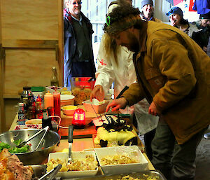 Jimmy cuts one of his birthday cakes. There are several people in the background watching the event