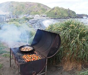 Australia Day — Wood fired BBQ just outside the boat shed. The BBQ is made up of two halves of a 200 litre drum. On the grill is kebabs and veggie patties in a large frying pan. Wireless Hill and the station buildings are in the background