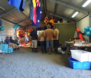 Australia Day — Four expeditioners standing on the sandy floor, watching an enthralling surf movie on a big screen TV set up in the boat shed