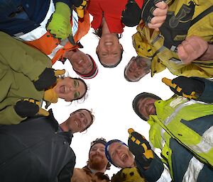 Australian team bonding session. Eight members of the team are standing in a circle. The image was taken from below, looking up at the circle of smiling faces