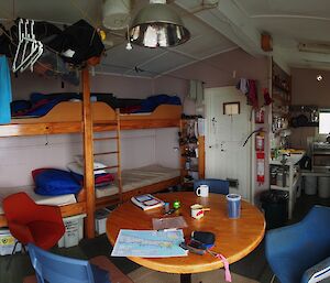 My home while down south — Hurd Point hut. A panoramic view of the inside of the hut, showing from the left, clothes hanging to dry, two double bunks on the back wall, table and chairs then through to the kitchen area and shelves stacked with food (on the far right)