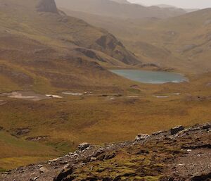 Only 27 kilometres to go back to station. The view is to the north from the track and shows many hills, the furtherest faded in the hazy air. There is a lake in the valley in the foreground