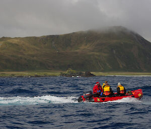 Eagle Shelter apple on the west coast as seen from the water. The shelter is seen in the distant background and is perched on a flat piece of ground about halfway up the escarpment. In the foreground on the water is one of the other IRB’s with four people onboard