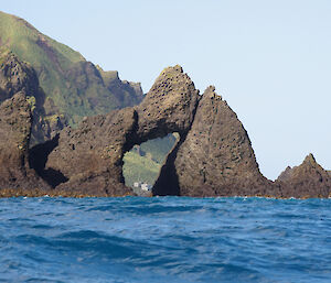 Hurd Point hut seen through the rocky arch offshore on the south coast. The steep slopes of the south coast escarpment can be seen in the background