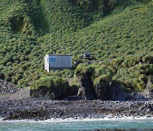 Hurd Point hut seen from an IRB just offshore from the beach. There is a colony of royal penguins just to the left of the hut, while the tussock mounds can be seen on the steep slopes behind the hut