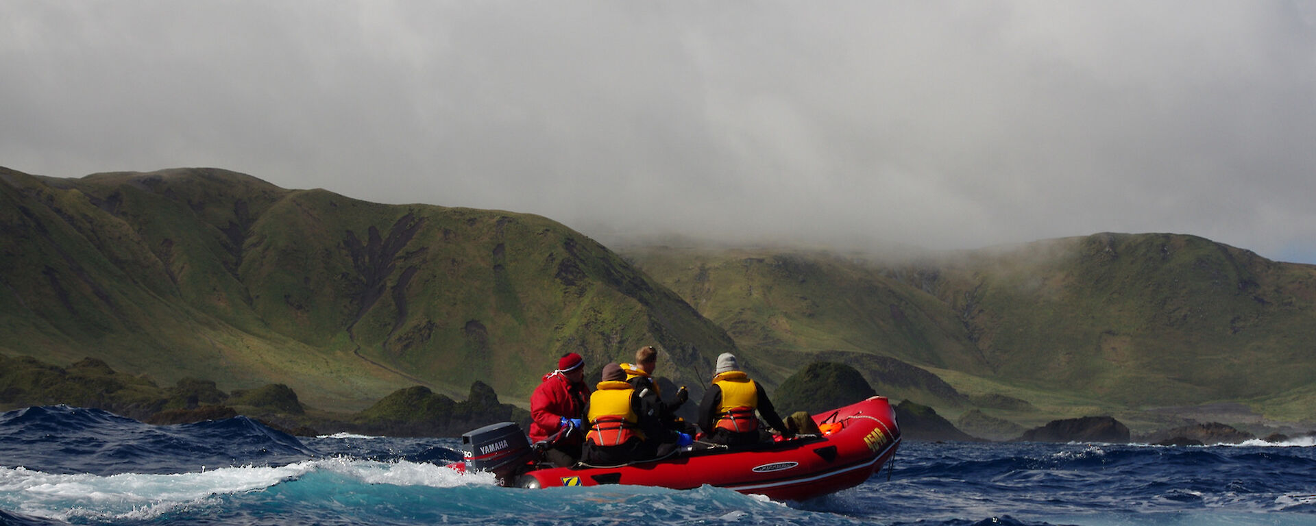 Cruising down the west coast. Image taken from an IRB with one of the other IRB’s in the foreground with four people on board. The rugged coast and green slopes of the escarpment are in the background