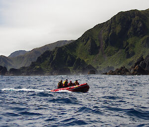 In the background are the rugged rock stacks along the southwest coast with the steep slopes of the escarpment rising up behind. In the foreground is an IRB with four people onboard