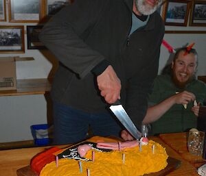 Greg cutting his cake which is in the shape of ‘big bird from Sesame Street