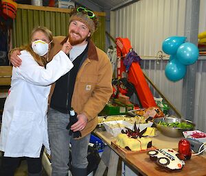 "Doctor’ Jaimie takes Jimmy’s pulse on his birthday. They are in the boat shed standing next to a table laden with food, including the two birthday cakes, one in the shape of an ambulance