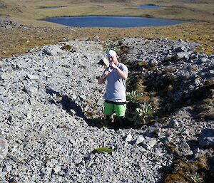 Josh inside the trench. The view is from the top of the trench on a sunny day with an unnamed lake in the background. Some cable can be seen coming out of the top of the trench