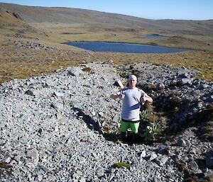 Josh standing in the trench at its deepest end. It is a sunny day and an unnamed lake can be seen in the background