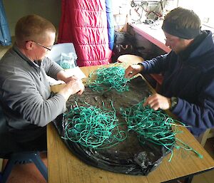 Chris and Kris in the Bauer Bay Hut counting pieces of green braided fishing line. There are 3 separate piles of the green fishing line