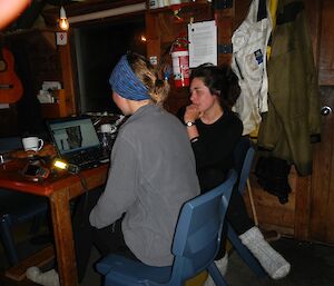 Karen and Laura sitting at the table at Green Gorge hut at night analysing the GPS track on a laptop computer