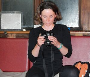 Kate, sitting on the lounge at Green Gorge hut at night, looking down onto the screen of a digital SLR camera analysing photo evidence