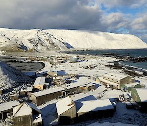 View of a snow covered station from halfway up North Head. The station is nestled in the foreground and in the background the snow covered escarpment with Handspike Point visible on the right