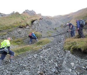 Kris and Chris hold the water pipe as Josh hammers in a new stake to secure it in place, Dave stands by supervising