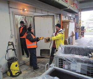 Three expeditioners move cargo from the pallet into the cold store
