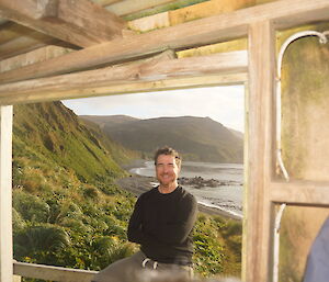 An expeditioner is in the hut door with a coastal bay behind