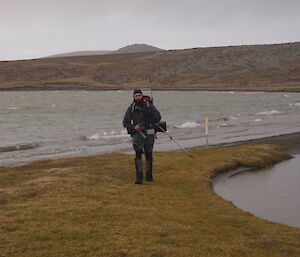 An expeditioner walking beside a lake