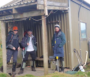 Three expeditioners stand outside a field hut