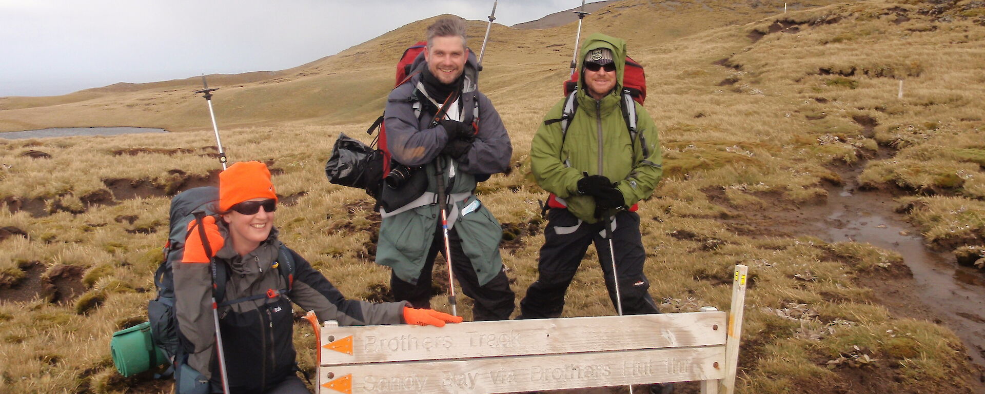 Three expeditioners pose beside a walking track sign