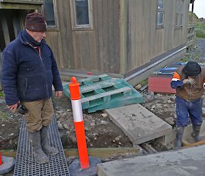 Two expeditioners workng beside a plumbing trench beside a station building