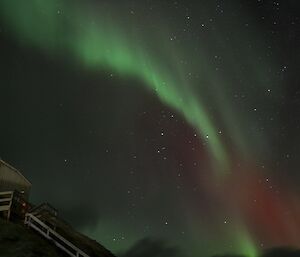 A large, bright aurora australis is seen hovering in the sky over a building on Macquarie Island