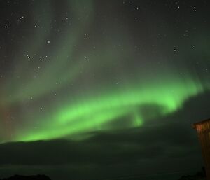 A brilliant, bright aurora australis dances over station buildings